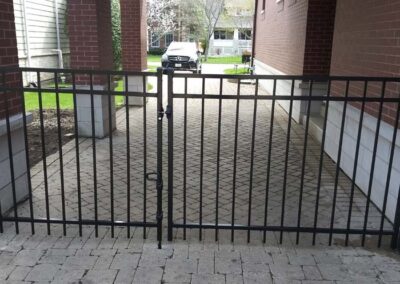 a black aluminum fence gate on a paver driveway