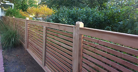 A custom wooden fence with wide horizontal slats in a backyard