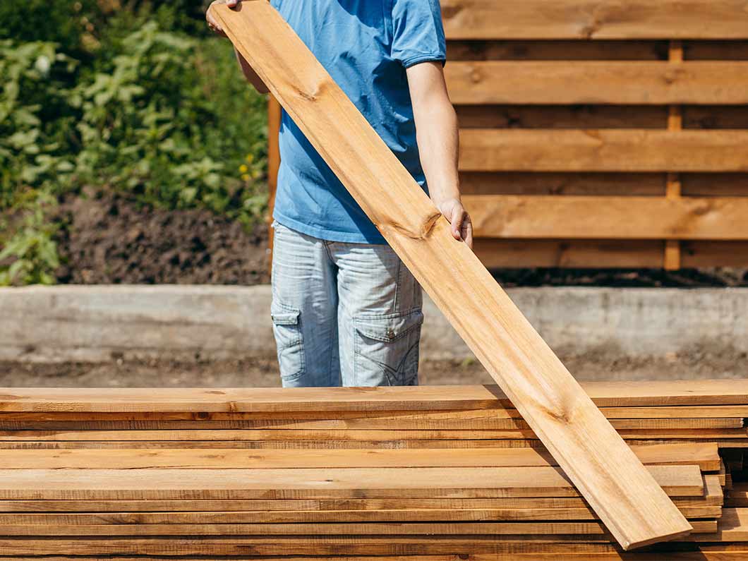 A man holding a wood fence plank, standing next to a wood fence construction project